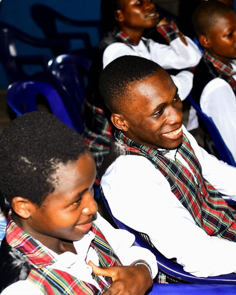 Two students in red tartan school uniforms smile as they listen to a talk at an event.